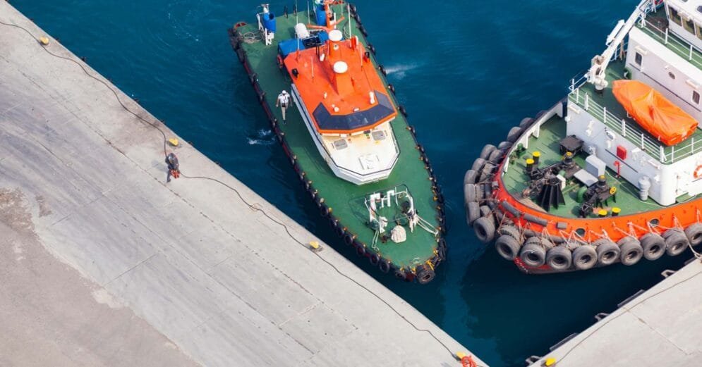an aerial view of two boats docked at a concrete pier.